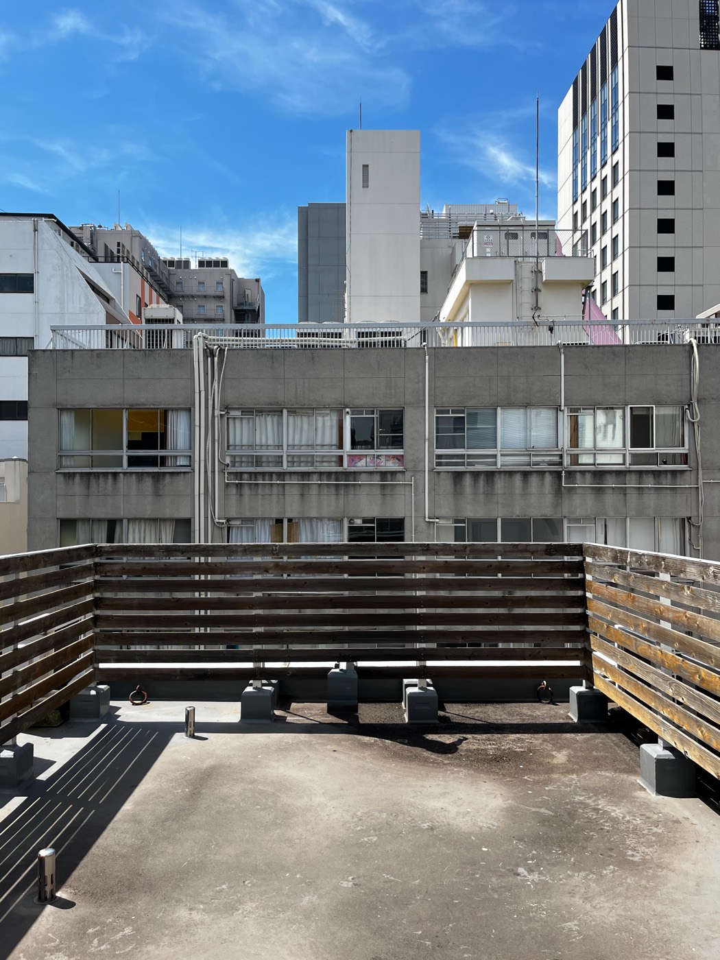 同じビルの屋上。木の柵に囲まれたコンクリートの床と、関内のビル群を背にした青空。